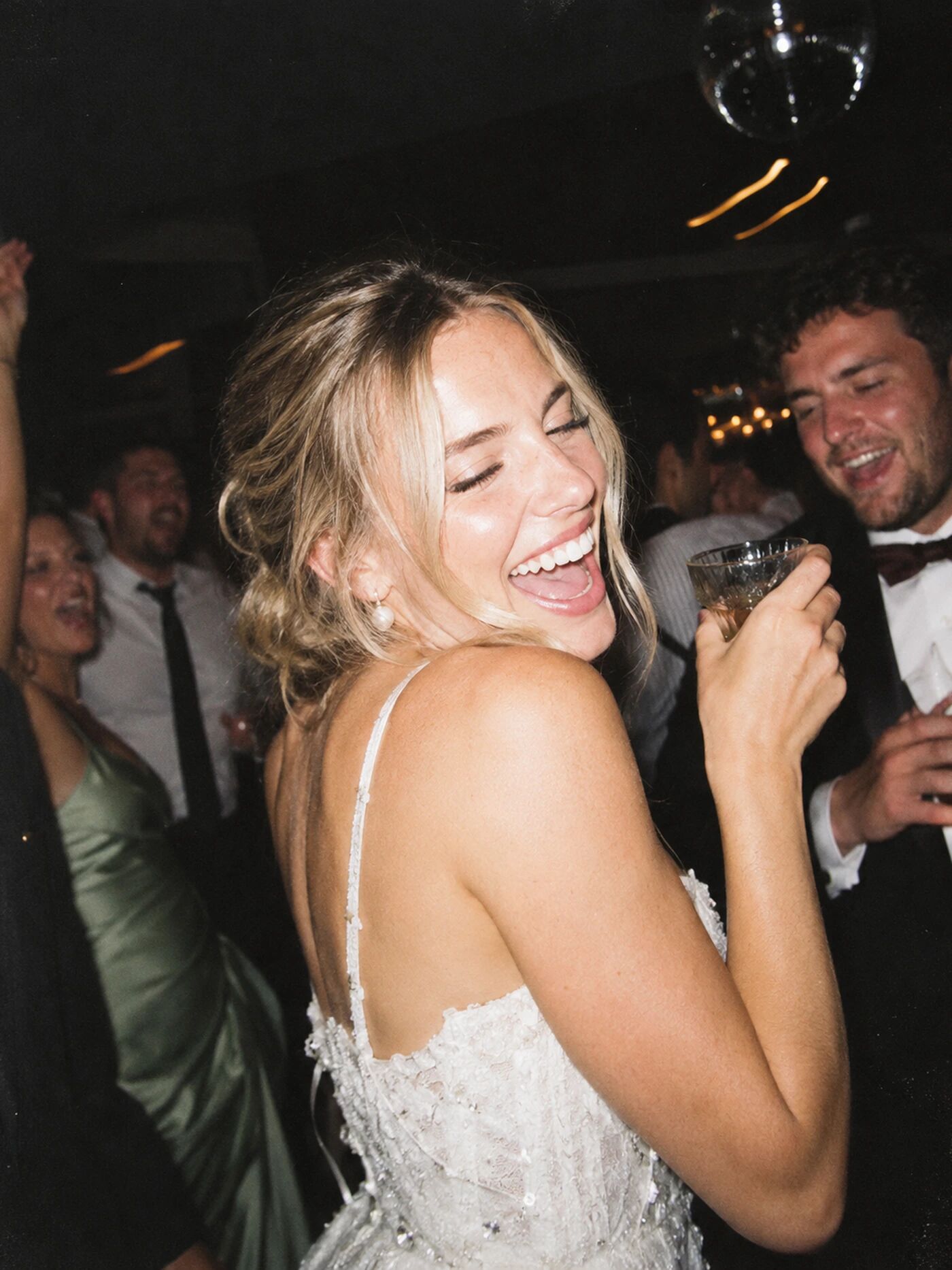 A bride mid-laugh, glass in hand, a groomsman behind her